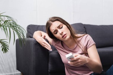 Kızgın kız sıcaktan acı çekiyor ve elinde bozuk klimanın uzaktan kumandası var.  