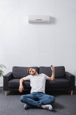 exhausted man feeling uncomfortable with broken air conditioner at home during summer heat  clipart