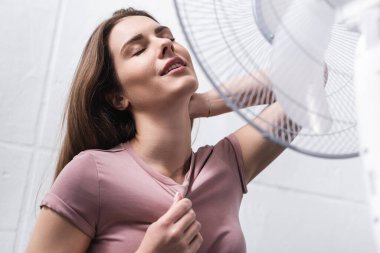 Güzel, mutlu bir kadın yaz sıcağında elektrikli vantilatörle rahat hisseder. 