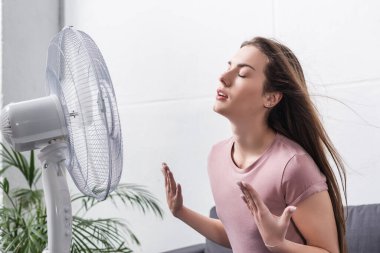 beautiful girl feeling comfortable with electric fan during summer heat clipart