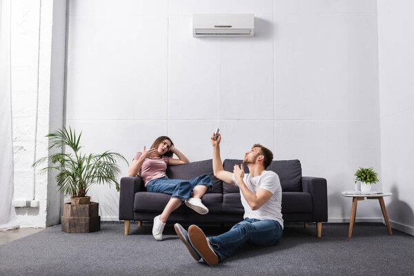 sad couple with remote controller at home with broken air conditioner 
