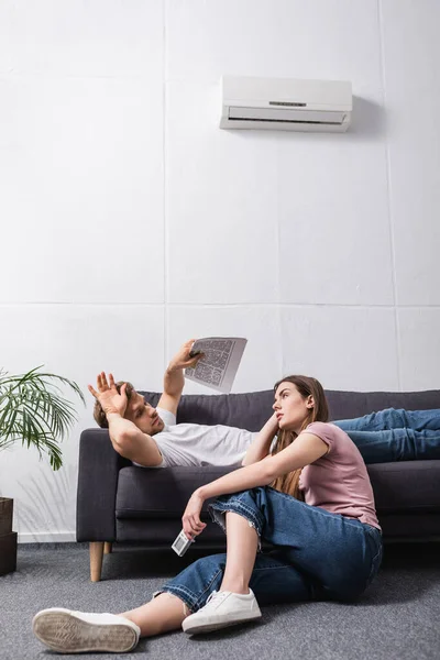 エアコンの故障で家で熱に苦しむリモコン付きの悲しいカップル — ストック写真