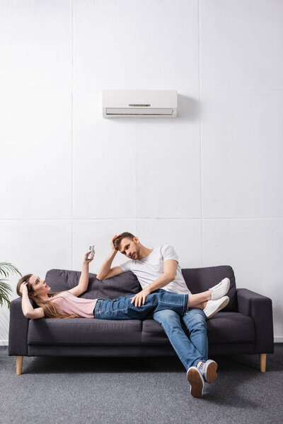 confused couple with remote controller suffering from heat at home with broken air conditioner 