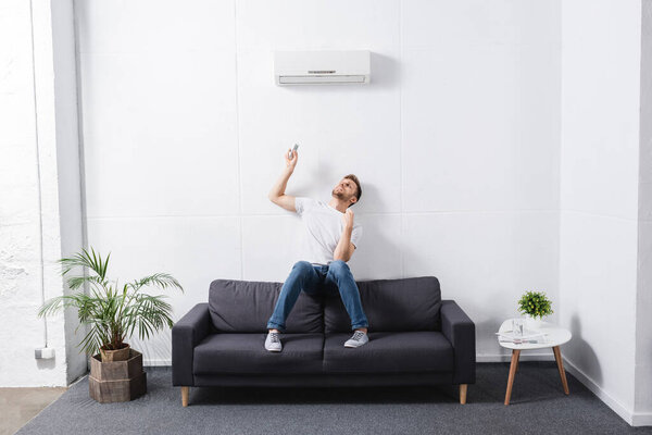 уставший человек держит пульт дистанционного управления и страдает от жары со сломанным кондиционером воздуха дома
 