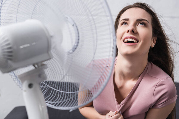 excited woman feeling comfortable with electric fan at home during summer heat