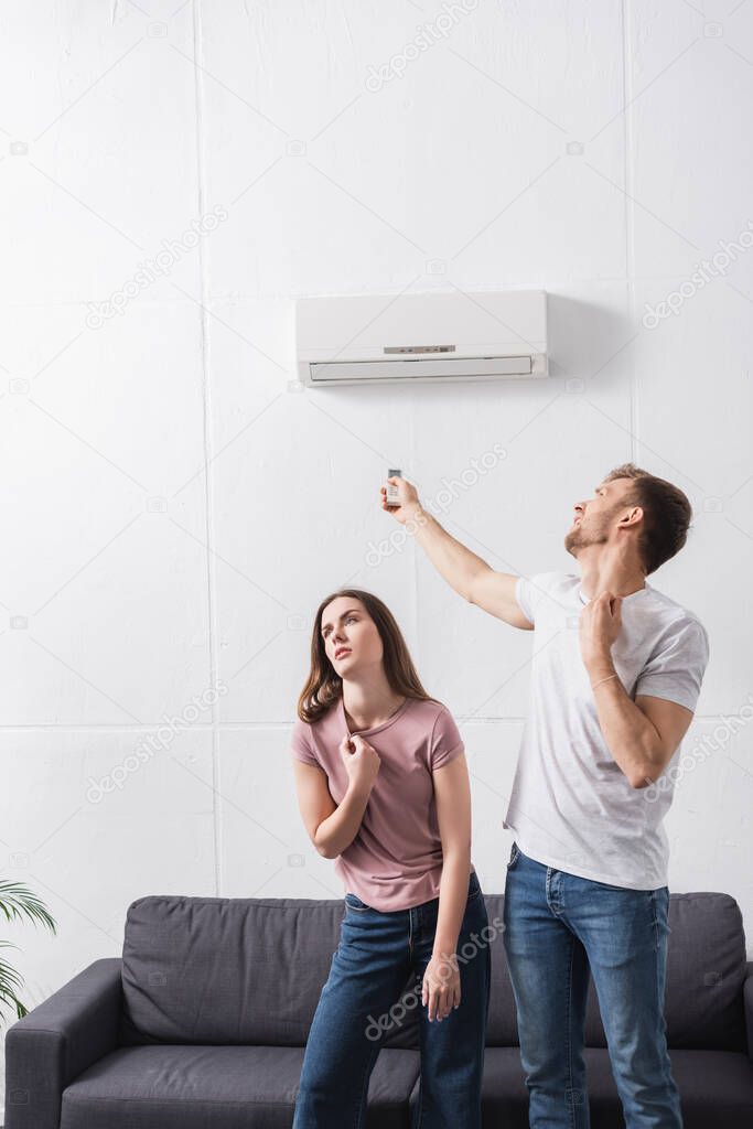 exhausted couple with remote controller suffering from heat at home with broken air conditioner 