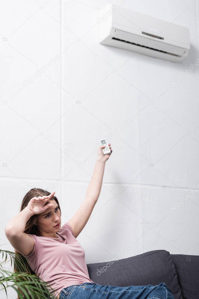 exhausted girl suffering from heat while trying to switch on air conditioner