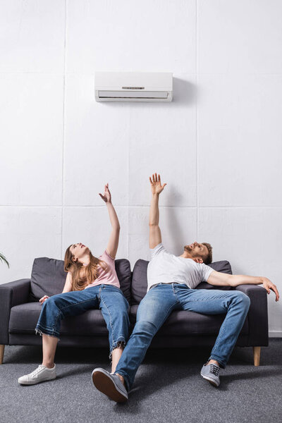 exhausted couple suffering from heat while sitting home with broken air conditioner 