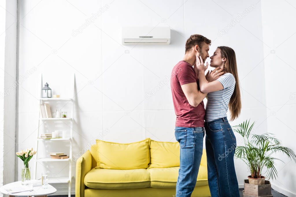 happy couple hugging and going to kiss at home with air conditioner