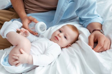 Yanında bebek şişesi tutan bir adamın, yatakta yatan sevimli oğlunun görüntüsü.