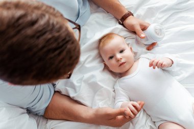 Baba, elinde sütle bebek şişesi tutarken, sevimli bir çocuğun yanında.