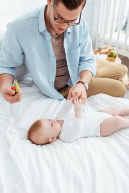 Küçük tatlı oğlunun ellerine dokunurken bebek çıngırağı tutan mutlu genç baba.
