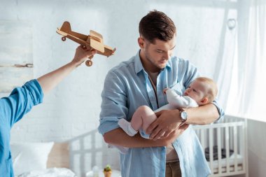 Babasının yanında oyuncak uçak tutan küçük sevimli kardeşi olan çocuğun kısmi görüntüsü.
