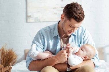 Mutlu genç baba, tatlı bebeği süt şişesiyle besliyor.