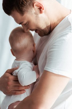 Neşeli, genç bir baba, kucağında küçük bir çocukla kucak açıyor.