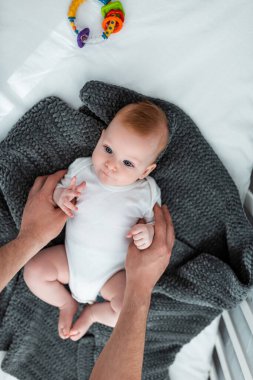Baba 'nın battaniyeye uzanmış küçük oğluna dokunuşunun kısmi görüntüsü