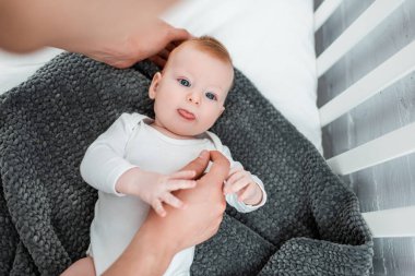 Bir adamın bebek karyolasında uzanan ve dilini dışarı çıkaran şirin bir çocuğa dokunuşunun görüntüsü.  