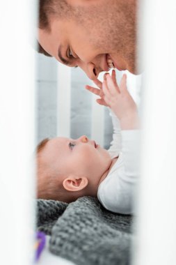 Bebek karyolasında uzanan ve gülümseyen babanın yüzüne dokunan sevimli erkek bebeğin seçici odağı.   