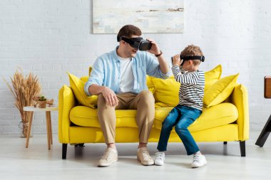 Gülümseyen baba ve oğul, sarı koltukta otururken birbirlerine bakıyorlar.