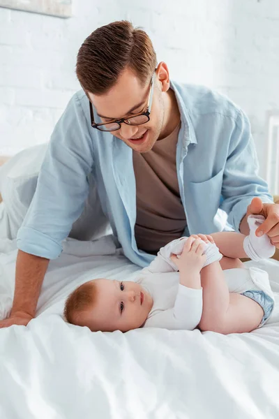 Feliz Jovem Pai Tocando Perna Adorável Pequeno Filho Deitado Cama — Fotografia de Stock