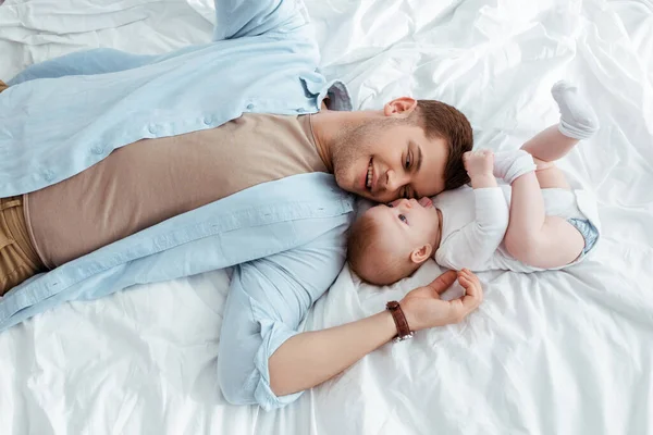 Gülümseyen genç bir babanın yatakta tatlı bir çocukla yüz yüze yatmasının en güzel görüntüsü.