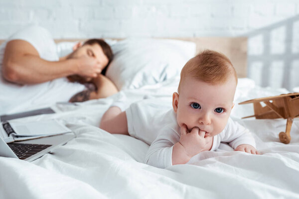 selective focus of cute infant crawling on bed neat tired father