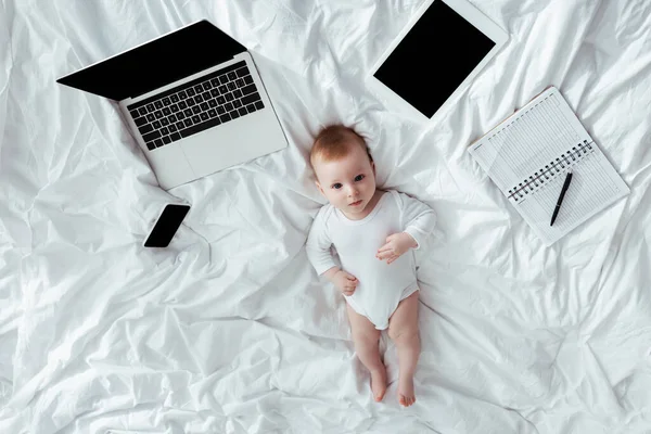 Top View Adorable Baby Boy Lying Bed Gadgets Notebook Pen — Stock Photo, Image