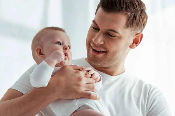 Sonriente Joven Sosteniendo Adorable Pequeño Hijo Las Manos Dormitorio —  Fotos de Stock