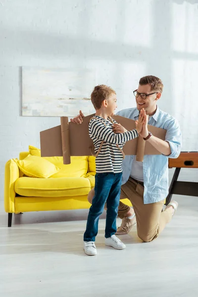 Lächelnder Vater Gibt High Five Glücklichen Sohn Mit Kartonflügeln Auf — Stockfoto