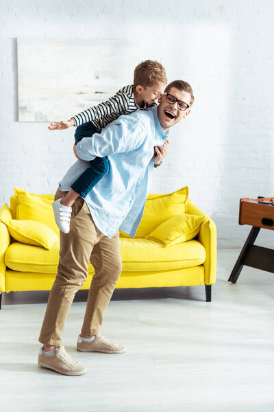happy father piggybacking cheerful son imitating flying
