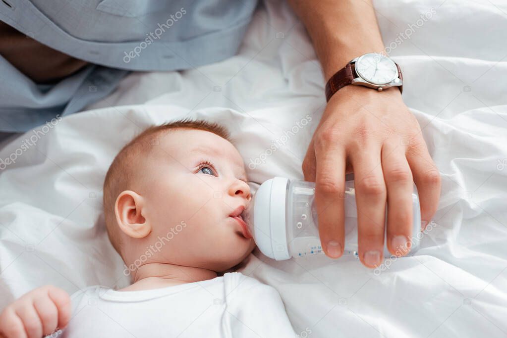 cropped view of father feeding cute little son from baby bottle with milk