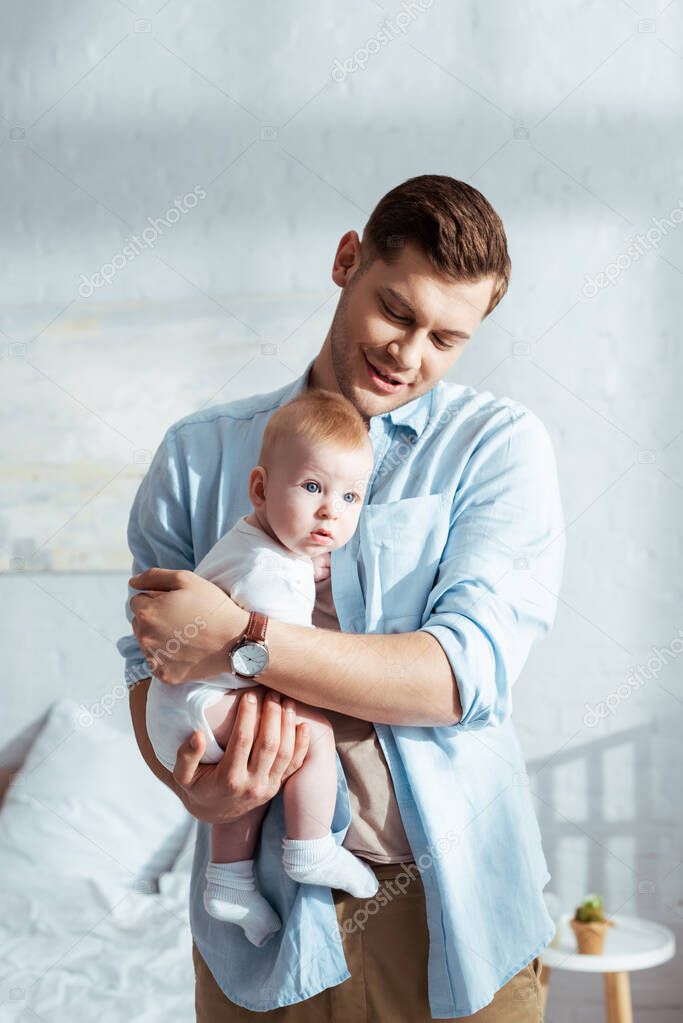 happy father holding adorable infant on hands in bedroom