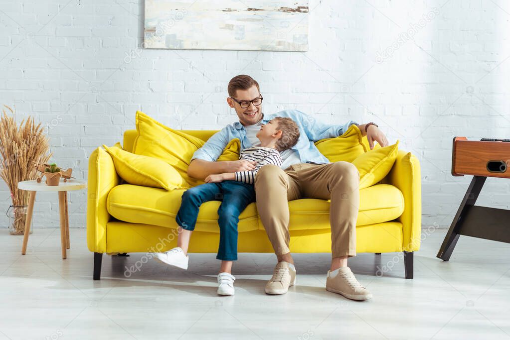cheerful father and son talking while sitting on yellow sofa
