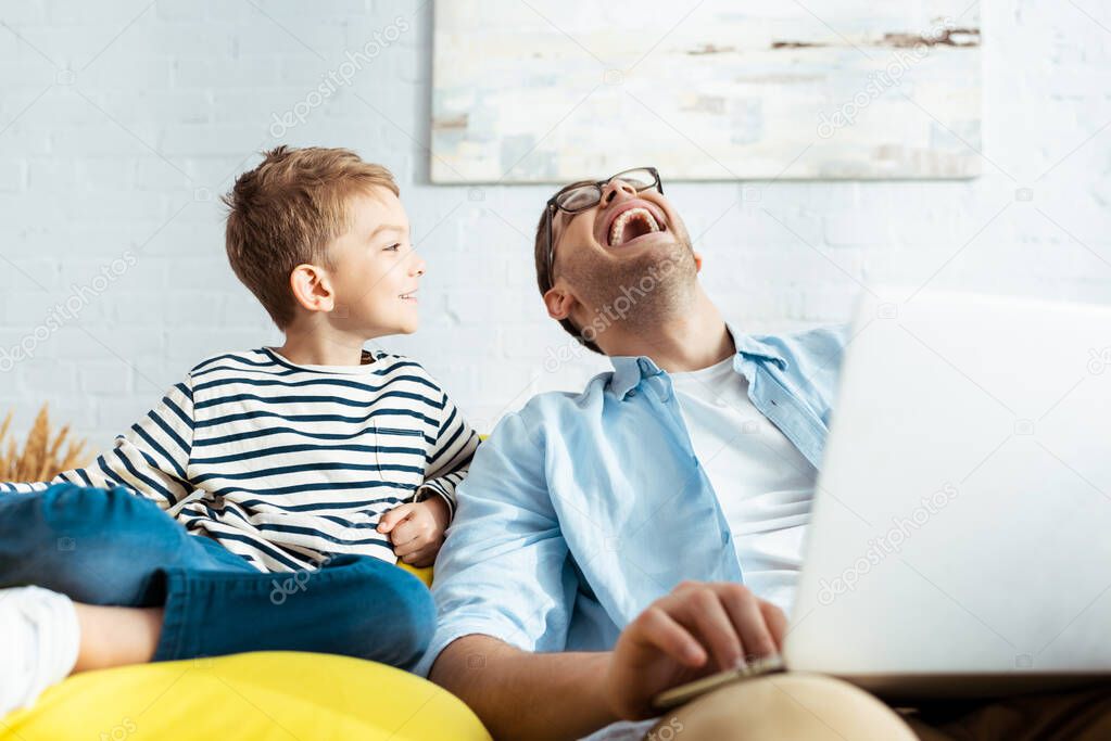 smiling boy looking at happy father using laptop