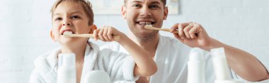 selective focus of happy father and son brushing teeth together, panoramic shot clipart