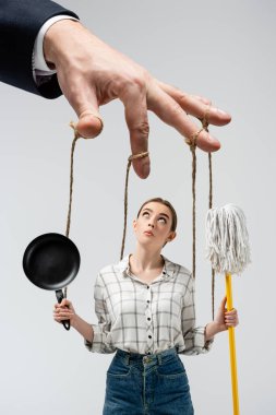 cropped view of puppeteer manipulating girl with mop and frying pan isolated on grey clipart