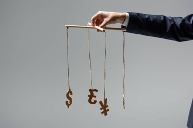 cropped view of businessman holding currency signs on strings isolated on grey clipart