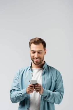 smiling young man using smartphone isolated on grey clipart