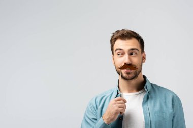 Takma bıyıklı komik bir genç adam. Gri üzerine izole edilmiş bir şekilde başka tarafa bakıyor.