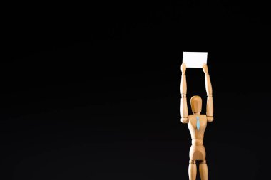 wooden marionette in tie holding blank placard isolated on black clipart