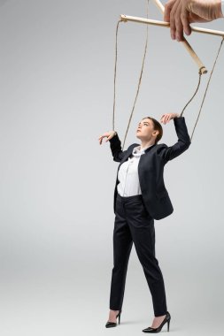 cropped view of puppeteer holding businesswoman marionette on strings isolated on grey clipart