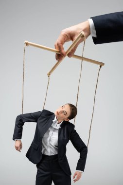 cropped view of puppeteer holding businesswoman marionette on strings isolated on grey clipart