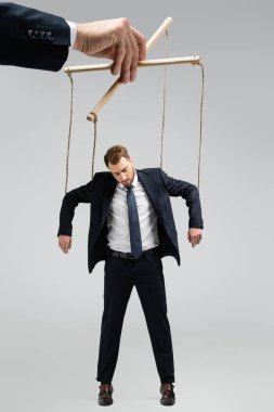 cropped view of puppeteer holding businessman marionette on strings isolated on grey clipart