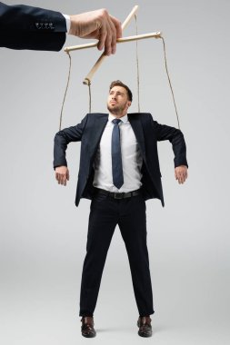 cropped view of puppeteer holding businessman marionette on strings isolated on grey clipart