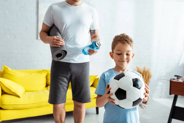看到一个人拿着健身垫和运动瓶子站在快乐的儿子身边 手里拿着足球 — 图库照片