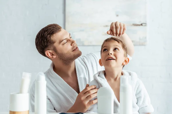 在浴室里 年轻父亲在梳妆台旁抚摩快乐儿子的头发 — 图库照片