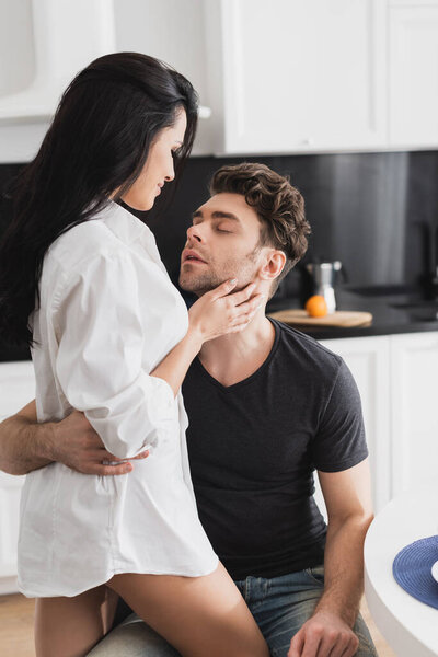 Sensual woman in shirt embracing handsome boyfriend in kitchen 