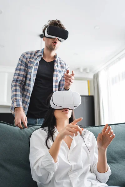 Young Couple Pointing Fingers While Using Virtual Reality Headsets Home — Stock Photo, Image