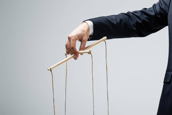 обрезанный вид кукловода, держащего марионетку изолированной на сером
