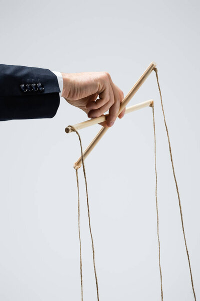 обрезанный вид кукловода в костюме, держащего марионетку изолированной на сером
